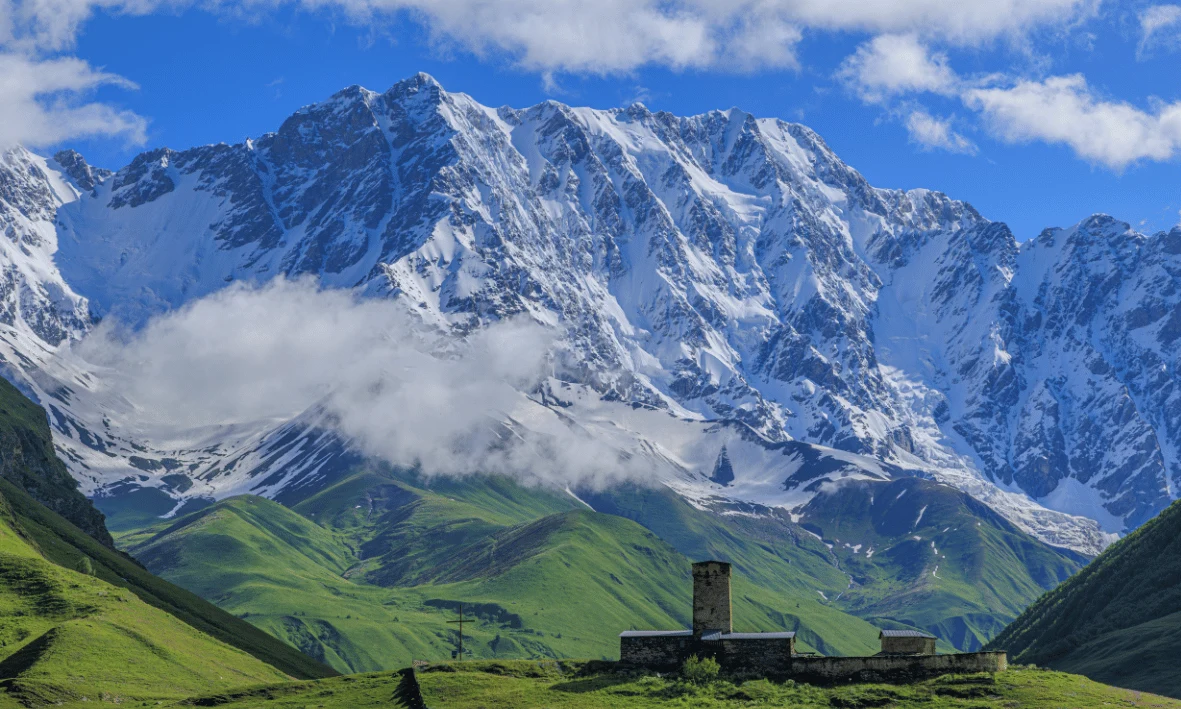 جبال القوقاز المغطاة بالثلوج في كازبيجي بجورجيا مع تلال خضراء في الأسفل خلال فصل الربيع