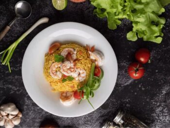 طبق Khao Pad التايلندي التقليدي من الأرز المقلي مع الروبيان والخضار ويُقدّم مع الليمون والبصل الأخضر