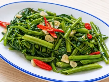 طبق Stir-Fried Morning Glory التايلندي مع الثوم والفلفل الحار على صحن أبيض بحافة زرقاء