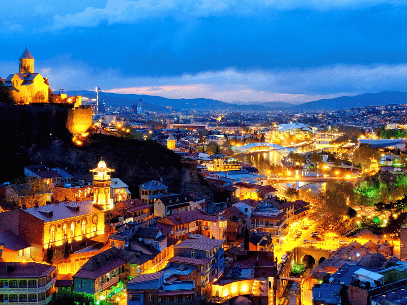 منظر ليلي لمدينة تبليسي أهم مكان في دليل جورجيا 2026 يظهر المدينة القديمة ونهر كورا وجسر السلام المضيء
