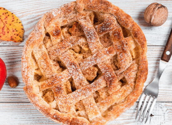 فطيرة التفاح الهولندية Appeltaart مع القرفة والتفاح الطازج على طاولة خشبية بأسلوب خريفي