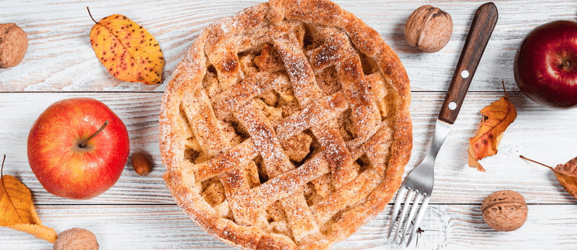 فطيرة التفاح الهولندية Appeltaart مع القرفة والتفاح الطازج على طاولة خشبية بأسلوب خريفي